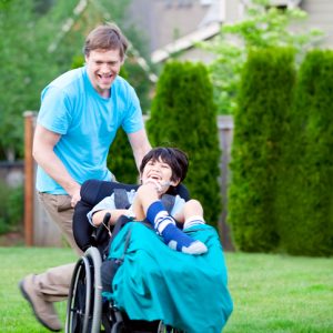 Father Racing Around Park With Disabled Son In Wheelchair