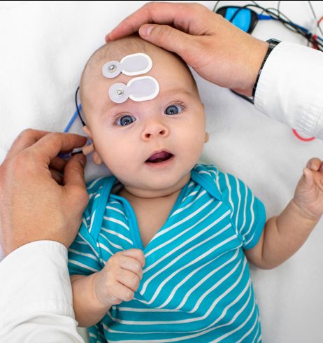 Newborn Hearing Screening And Diagnosis At The Hospital. Baby Having Hearing Screening With Special Electrodes On His Head And Ear